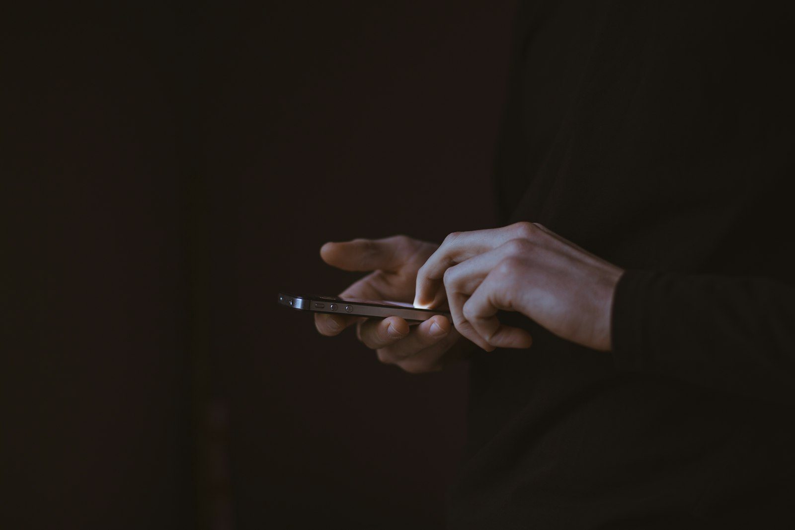 Manos sosteniendo un teléfono móvil en la oscuridad